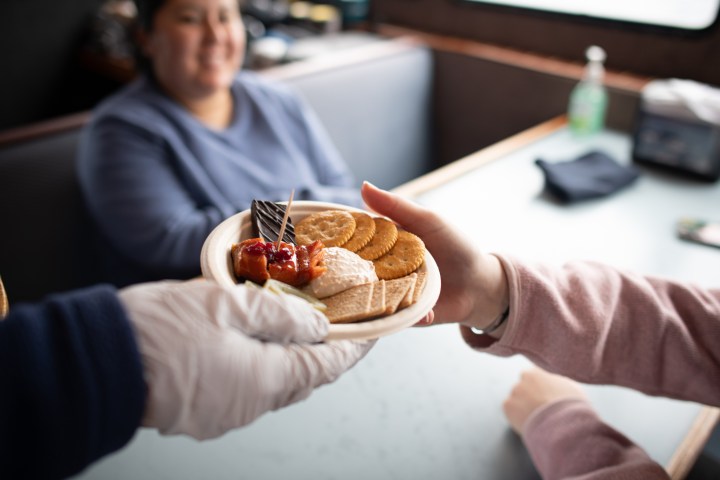 Deckhand hands a snack plate with crackers, salmon dip, chocolate, and kelp pickles to a guest across a table.