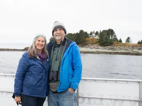 a man and a woman standing next to a body of water in front of a lighthouse