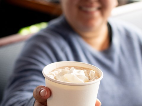 Person in blue shirt holding a cup of hot drink with whipped cream in focus.